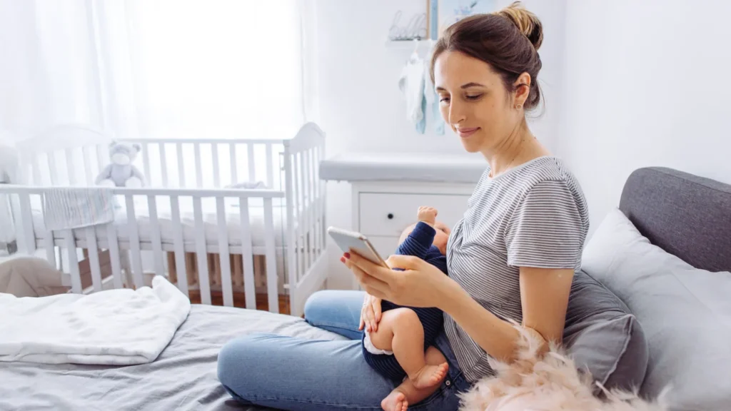 A photo of a woman feeding her infant while looking at her phone